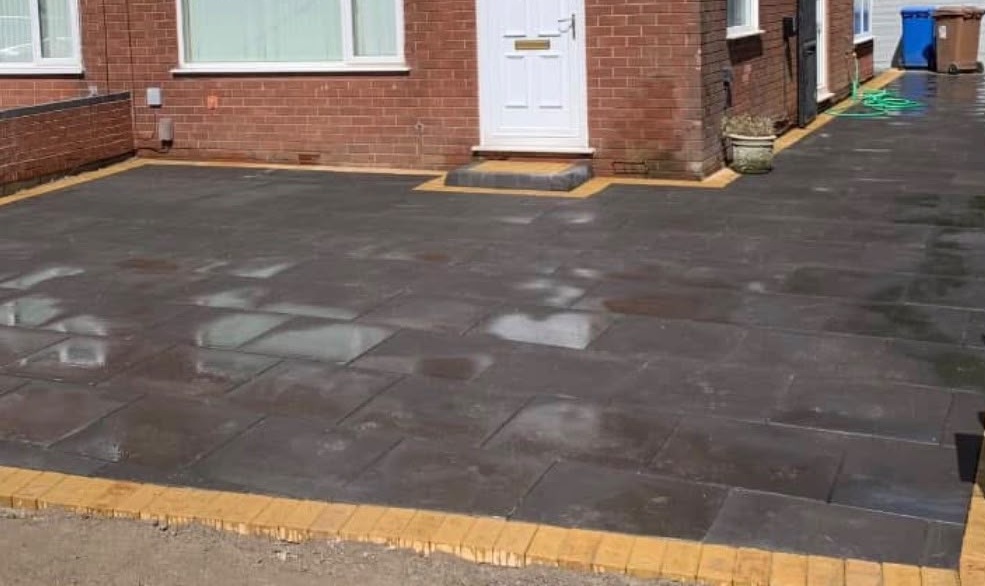 Grey flagged front driveway with buff brick edging on a brick house