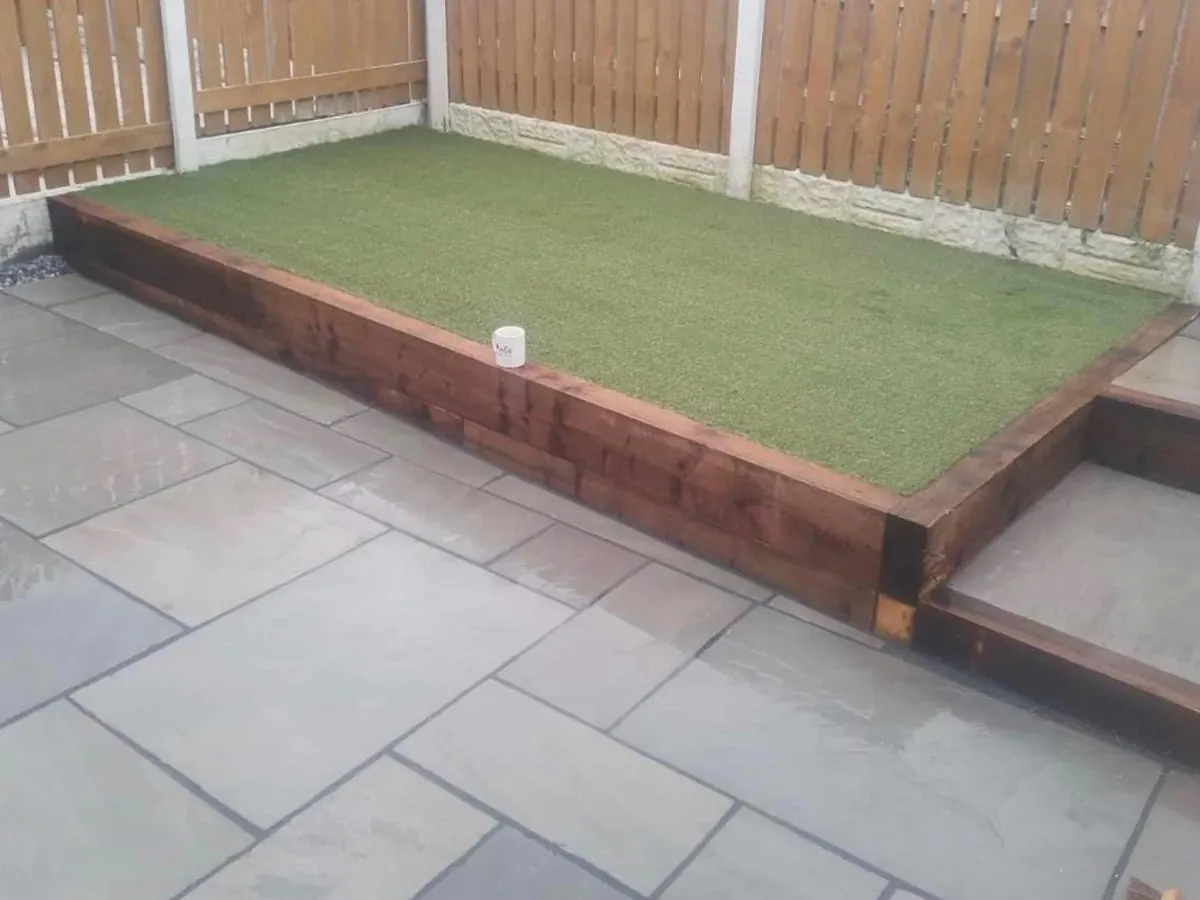 Raised sleeper bed of artificial grass beside grey patio flags