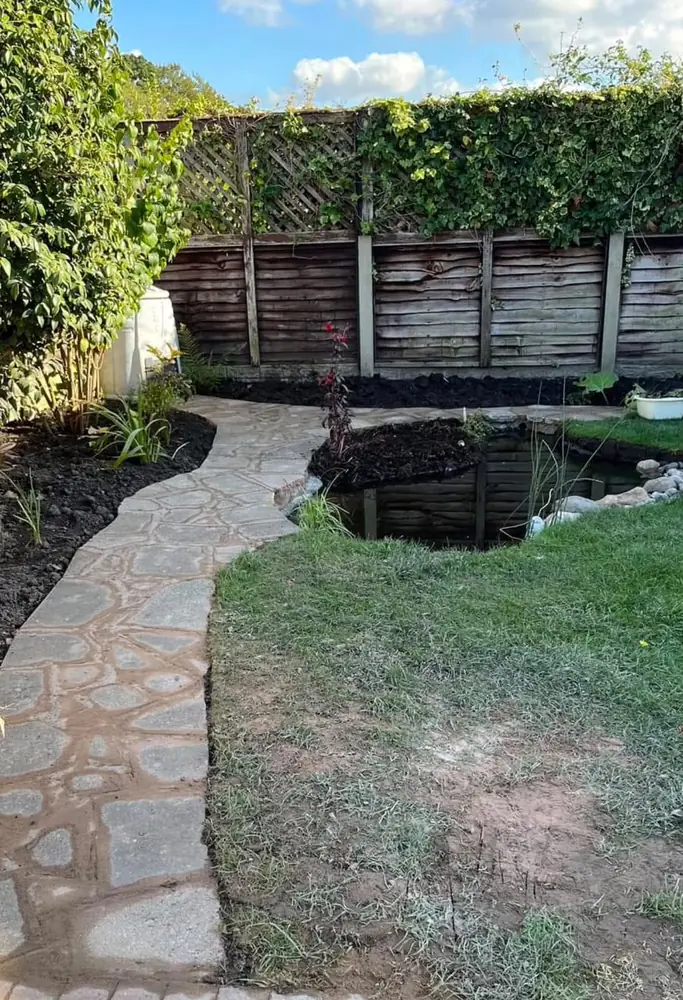 Garden pond with stone path, planting and a timber fence