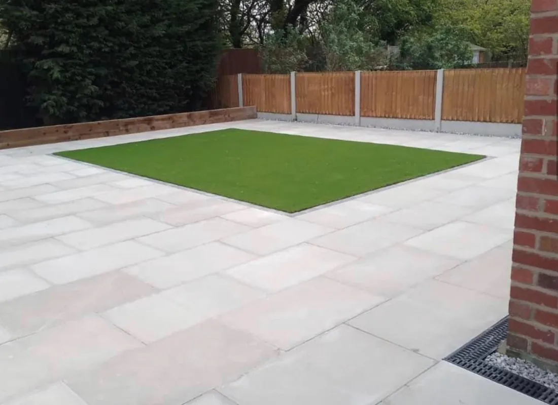 Light stone patio with a square of lawn and timber fence