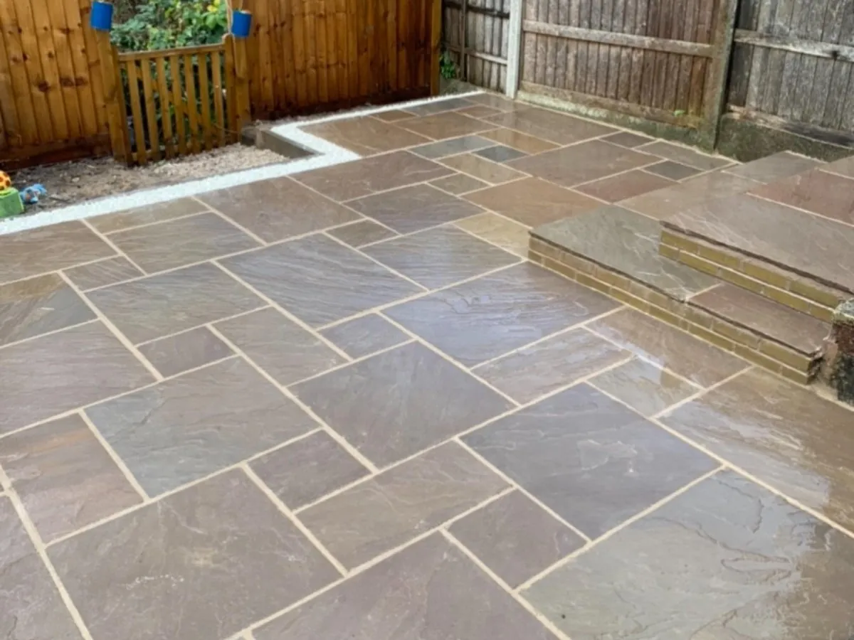 Mixed stone patio with brick steps and timber fencing in a back garden