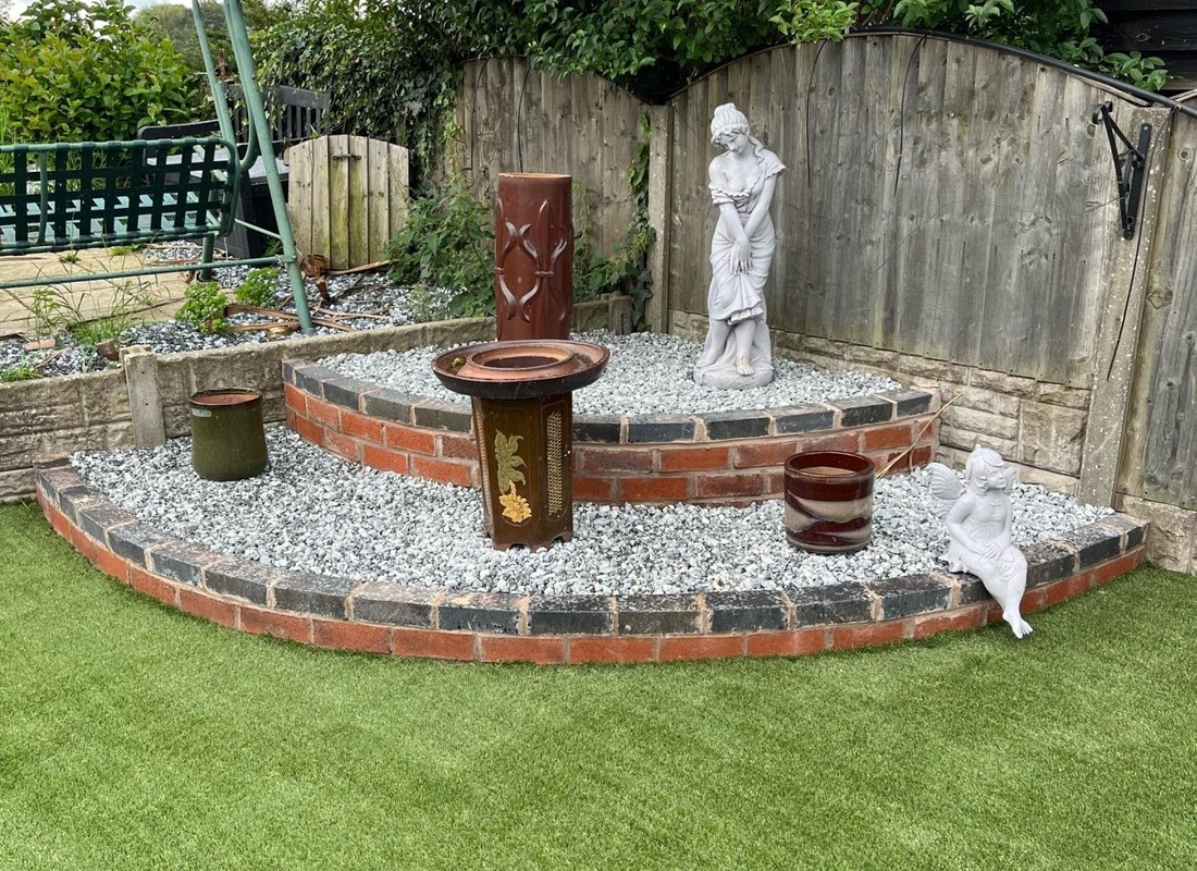 Curved brick planter with gravel, statues and lawn